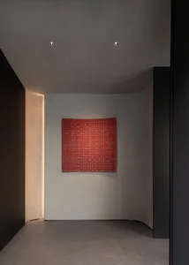 Minimalist curved hallway with smooth micro-cement walls, dark accent wall, recessed lighting, and a large square red woven textile artwork centered on the back wall.