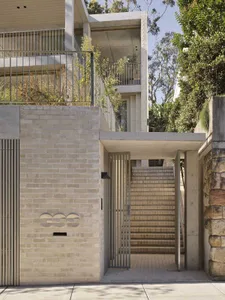 Modern concrete and brick house entrance with vertical metal gate, outdoor staircase, and integrated greenery on multiple levels.