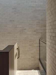 Modern minimalist staircase with light-colored brick walls, dark wood and metal handrail, and limestone steps.