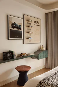 Modern bedroom corner with a teal floating console shelf displaying books and model cars, a woven stool, framed automotive art, and a curated car collection display on the wall.
