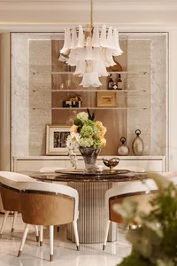 Luxurious dining room with round dark marble table, white and tan upholstered chairs, large floral chandelier, and marble wall with decorative shelving.