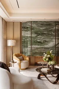 Modern luxury living room with large green marble feature wall, gold velvet swivel armchair, white curved sofa, and dark marble coffee table with floral arrangement.