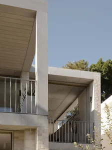Modern concrete building exterior featuring a second-floor balcony with stainless steel railings, integrated planter box with snake plants, and dramatic architectural overhangs against a clear sky.