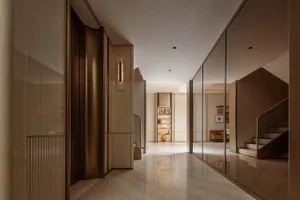 Modern luxury hallway with floor-to-ceiling brass mirrored cabinetry, fluted wall panels, polished marble floor, and integrated vertical lighting.