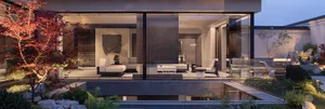 Modern luxury villa living room with floor-to-ceiling glass walls opening to a landscaped garden featuring a red Japanese maple, travertine fire pit, and minimalist outdoor furniture at dusk.