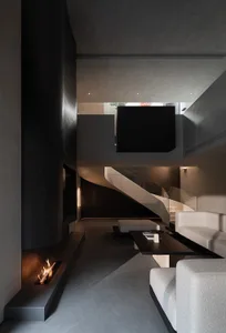 Modern double-height living room featuring a dramatic black micro-cement fireplace, floating staircase, light grey modular sofa, and dark coffee table under high ceilings.