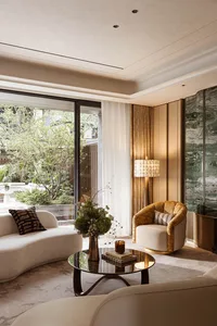Modern luxury living room featuring a curved white sofa, golden velvet swivel armchair, round black marble coffee table, large green marble feature wall, and floor-to-ceiling glass doors opening to a lush garden.