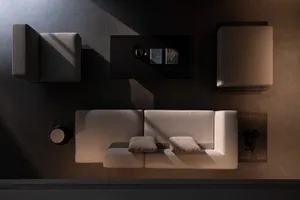 Top-down view of a minimalist living room featuring a beige boucle modular sofa, dark wood coffee table, and two armless accent chairs on a dark concrete floor with strong natural light casting bold shadows.