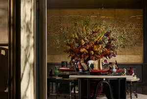 Luxurious entryway console table featuring a massive autumnal floral arrangement with dried flowers and branches, set against a hand-painted gilded Chinoiserie screen, with black lacquered furniture and porcelain accents.