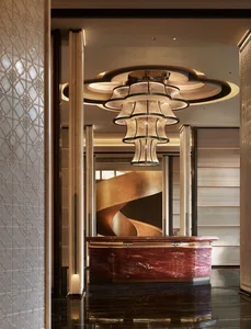 Luxurious hotel lobby featuring a curved red marble reception desk, dramatic multi-tiered chandelier, and a sweeping golden spiral staircase in the background.