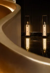 A sophisticated luxury lobby featuring a sweeping curved marble wall with integrated lighting, paired with two illuminated glass display cases showcasing ceramic vases on marble pedestals, all reflected in a highly polished dark marble floor.