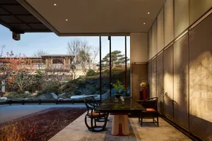Modern Chinese-style dining room featuring a black marble dining table, traditional-inspired chairs, folding screen panels with ink-wash landscape paintings, and a large opening revealing a classical Chinese garden with red plum blossoms and rockery.