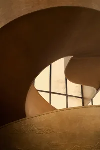 Close-up view of a sculptural bronze spiral staircase featuring smooth curved forms and traditional Chinese cloud and mountain embossed patterns.