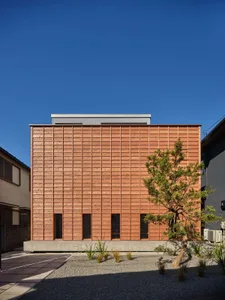 Modern two-story house completely clad in horizontal cedar wood panels, elevated on a concrete base, with a Japanese-style gravel garden and pruned pine tree in the foreground.