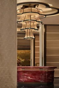 Luxurious hotel or corporate reception desk made of deep red marble with gold accents, topped by an elaborate multi-tiered beige and teal chandelier with intricate detailing.