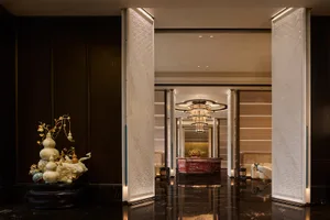 Luxurious hotel lobby entrance with dark marble floors, white patterned wall panels, a large traditional Chinese gourd sculpture, and a red marble reception desk in the background.