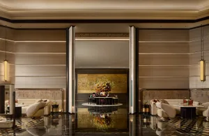 Luxurious hotel lobby featuring high-gloss black marble floors, beige curved sofas, golden floral centerpiece, and backlit wood-paneled walls.