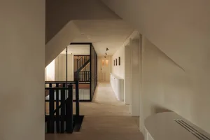 Modern minimalist upper hallway with light oak wood flooring, white walls, black metal railings, and built-in white storage units.