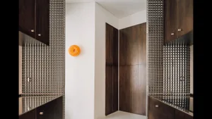 Modern minimalist entryway featuring dark wood cabinetry, silver mosaic tile walls, white walls, and a bright orange circular wall light fixture.