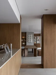 Modern minimalist dining room featuring rich walnut wood paneling, a solid wood dining table, concrete floor, and a white sculptural wall art installation made of circular forms.