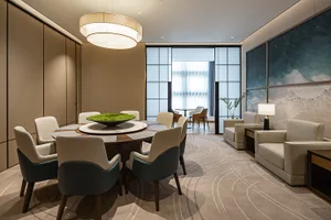 Modern executive meeting room with a large round walnut conference table, cream and teal leather chairs, a cylindrical chandelier, and ocean wave artwork on the wall.