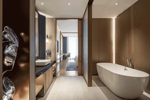 Modern luxury ensuite bathroom with a white freestanding bathtub, walnut wood paneling, vessel sink on dark countertop, and view through to the bedroom.