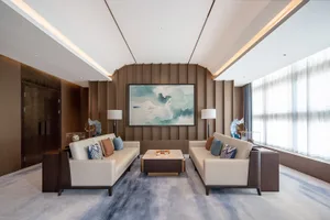 Modern Chinese living room with two cream sofas facing each other, a curved walnut wood feature wall, large abstract jade landscape painting, marble coffee table, and blue-grey area rug.