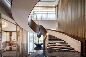 Double-height luxury lobby featuring a dramatic curved black marble staircase, a large teardrop pendant light, and reflective polished marble floors.