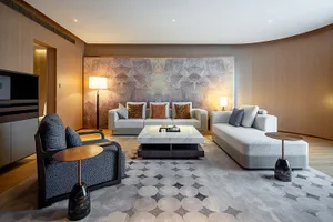 Modern luxury living room with curved wooden walls, large marble coffee table, light gray L-shaped sectional sofa, blue patterned armchair, and dramatic textured feature wall with warm lighting.