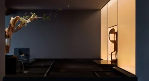 Modern minimalist meditation room featuring a large sculptural driftwood installation, flowing water feature, dark charred wood platforms, and warm backlit onyx wall panels.