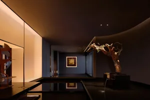 Modern dark hallway featuring a large sculptural dead tree installation, reflective black floor, curved ceiling, and warm backlit wall panels.