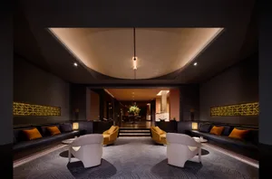 Modern luxury hotel lobby with white curved lounge chairs, golden yellow armchairs, navy blue velvet banquettes with orange pillows, dramatic cove lighting and geometric gold wall accents.