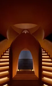 View looking up through a series of large terracotta-colored arched openings with integrated warm LED lighting along the edges of the staircase steps.