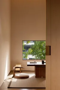 A serene Japanese minimalist home office featuring a walnut desk, round wooden chair with cushion, tatami mat, and a large window overlooking green trees.
