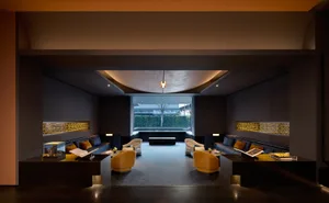 Modern luxury hotel lobby lounge featuring dark stone walls, curved ceiling, mustard yellow swivel chairs, deep blue sofas, and golden lattice light fixtures.
