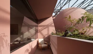 Modern rooftop terrace in warm terracotta tones with a large curved planted dome, wooden armchair, and dramatic natural light patterns.