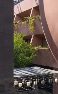 Modern architectural courtyard featuring terracotta-colored concrete walls, hanging ferns, and a grid of concrete pavers with integrated lighting below.