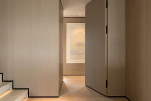 Modern minimalist hallway featuring light oak wood paneling, a framed landscape painting at the end, and warm LED step lighting.
