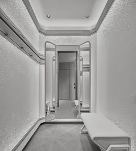 Modern minimalist dressing room with white textured plaster walls, geometric patterned carpet, white upholstered bench, and multi-panel mirrored doors reflecting the space.