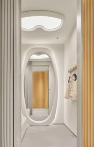 Modern minimalist hallway with white organic-shaped arched doorway, light oak wood paneling, and soft neutral textiles.