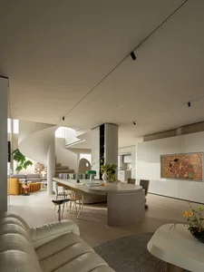 Modern open-plan living room featuring a dramatic white spiral staircase, curved light oak kitchen island with bar stools, cream leather sofa, and large Klimt-style artwork on the wall.