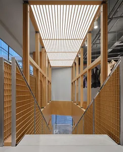 View looking up a modern double-height staircase constructed with light oak wood slats and metal railings, featuring a long linear skylight above and hanging coats on the upper level.