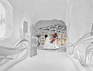 Modern ski retail store interior designed as a white snow cave with organic curved plaster walls, ski equipment display, and a mannequin skier in colorful winter gear.