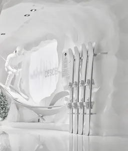 Modern all-white retail display featuring a ski rack with white skis, a skier snow sculpture on a ramp, and organic curved white cave walls with recessed lighting.