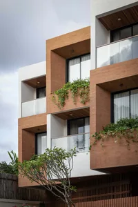 Modern residential building exterior featuring terracotta brick cladding, white concrete walls, large glass windows, and lush green vines cascading from balconies under an overcast sky.