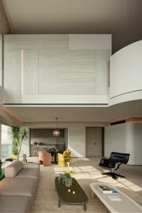 Modern double-height living room featuring light wood paneling, a curved white wall, beige sectional sofa, black leather lounge chair, and colorful yellow and terracotta accent chairs in an open-plan layout.