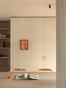 Modern minimalist dining area with light oak table, two wooden chairs, open book, amber glass, built-in beige cabinetry and a colorful portrait painting on the wall.