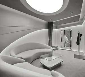Modern futuristic white boutique interior with sweeping curved white leather sofas, a square glass coffee table filled with glowing quartz crystals, dramatic circular ceiling light feature, and full-length mirrors.