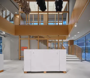 Modern double-height retail interior with light oak wood structural beams, white walls, concrete floor, and clothing hanging from the ceiling.