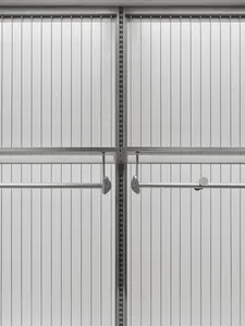 Close-up view of a minimalist white closet interior featuring vertical fluted panels, adjustable stainless steel hanging rods, and decorative metal hooks.